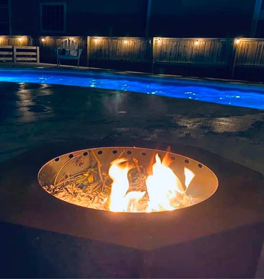 Backyard swimming pool with fire pit and nighttime lighting
