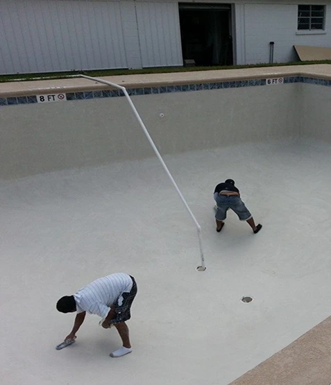Workers applying new surface finish during in ground pool replastering renovation